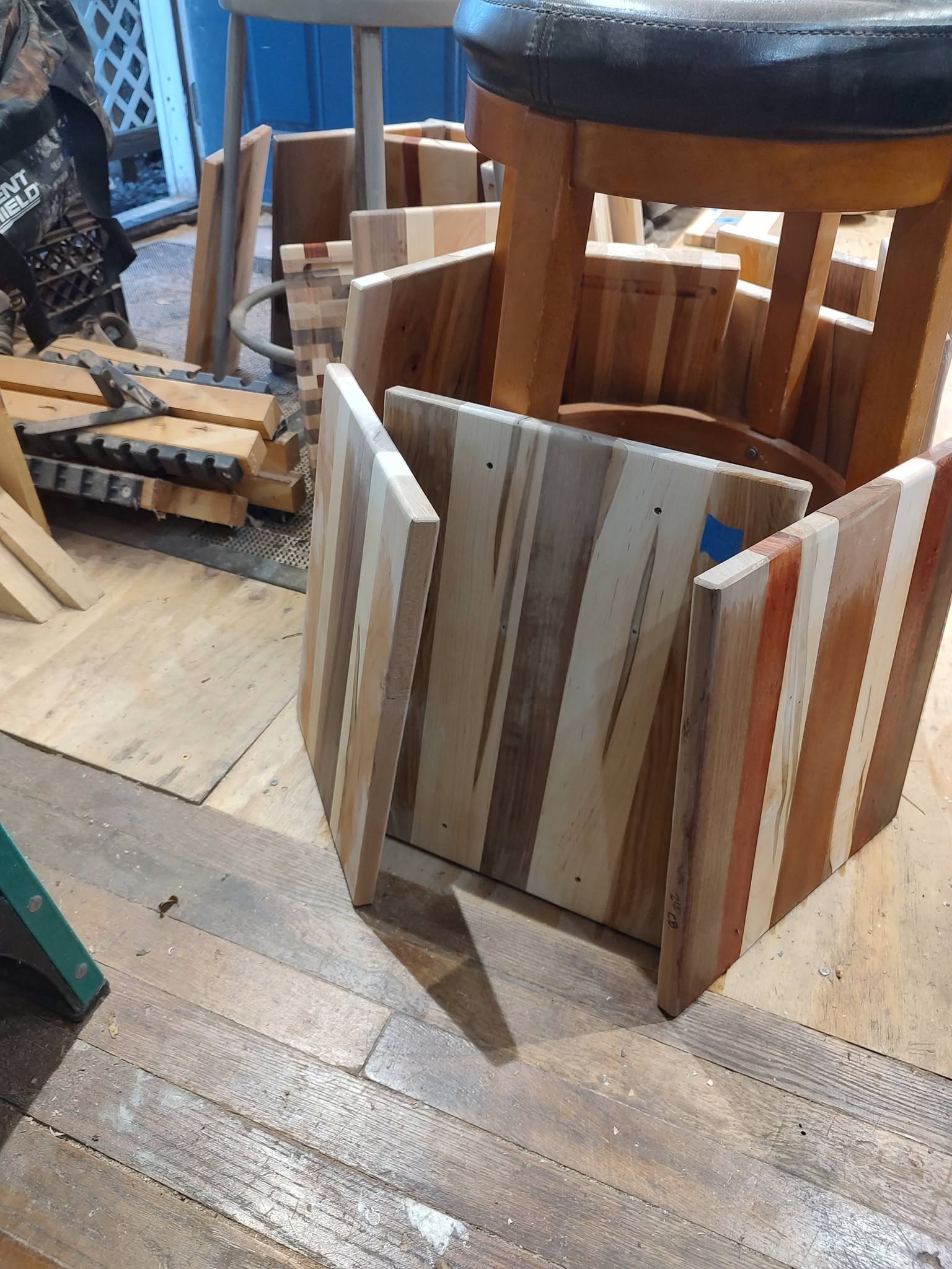 Hardwood boards with varied grain and color standing beside stools in the woodworking shop